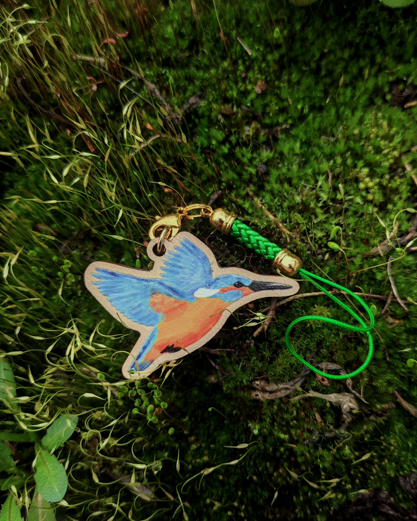 A wooden charm of a kingfisher on green moss.