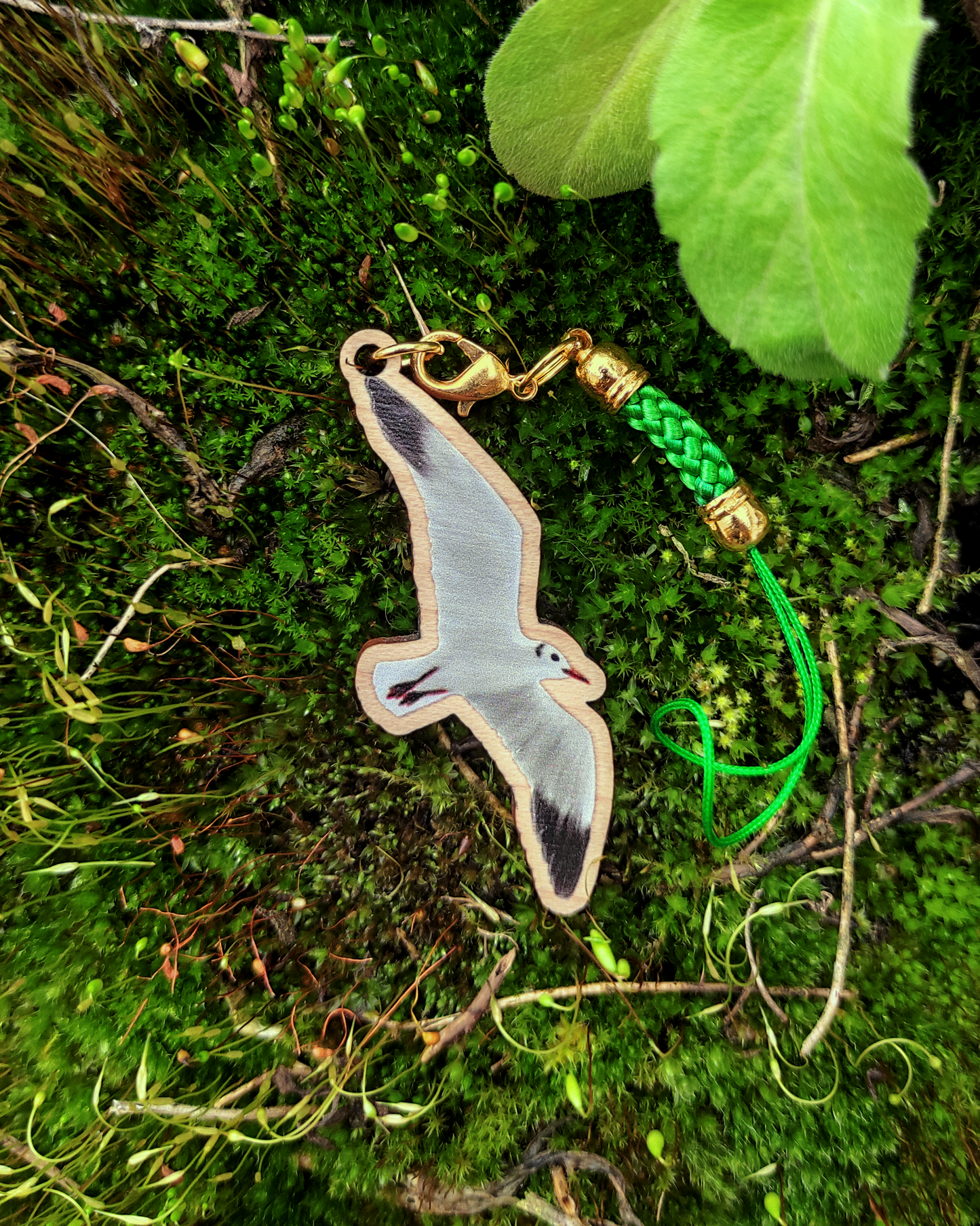 Wooden charm of a black-headed gull on a moss background