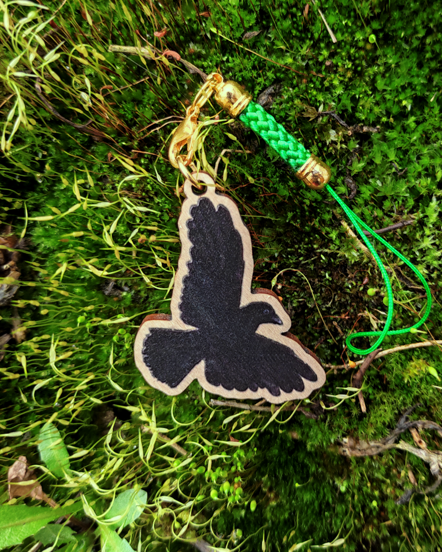 Wooden charm of a Carrion Crow on mossy background.