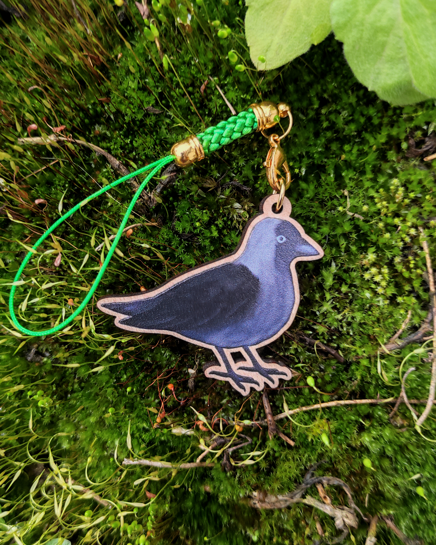 Wooden charm of a Jackdaw on mossy background.