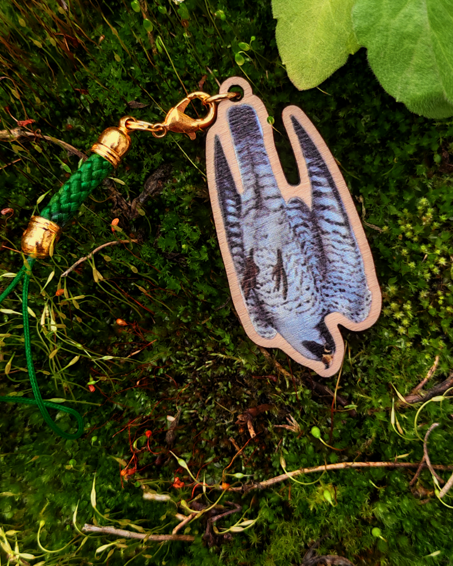 Wooden charm of a Peregrine Falcon on mossy background.