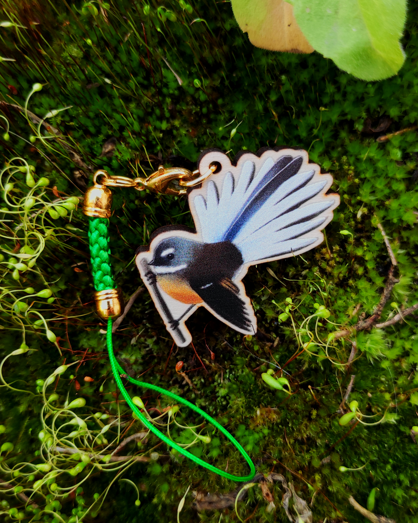 Wooden charm of a New Zealand Fantail on mossy background.