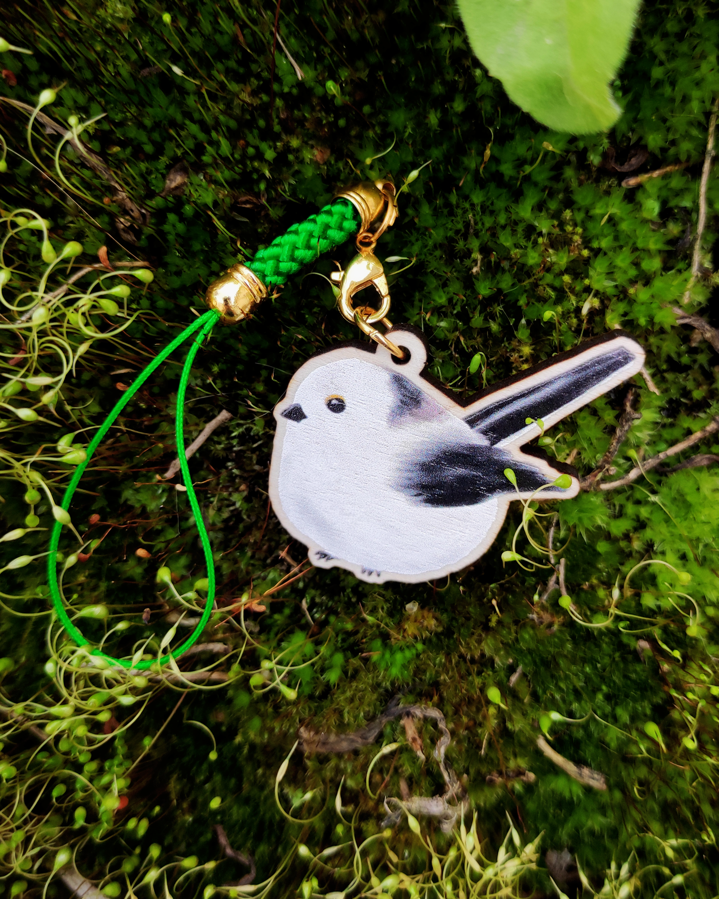 Wooden charm of a Long-tailed tit on mossy background.