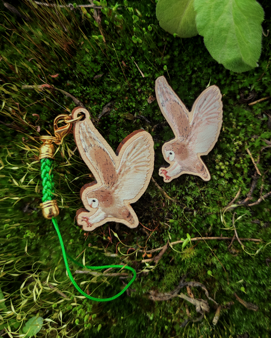 Wooden pin and charm of a Barn Owl on mossy background.