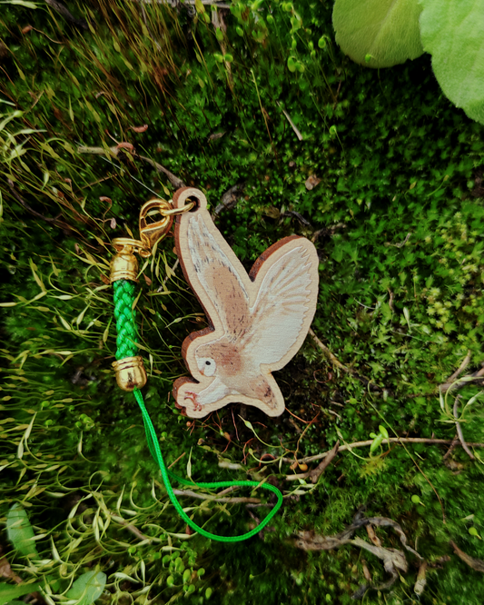 Wooden charm of a Barn Owl on mossy background.