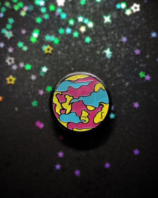 Hard enamel pin of a stylized planet on a dark, blurry background. The pin has the colors of the pansexual flag in it.