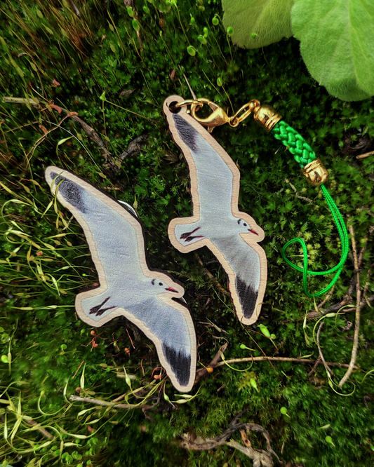 Wooden pin and charm of a black-headed gull on moss background.