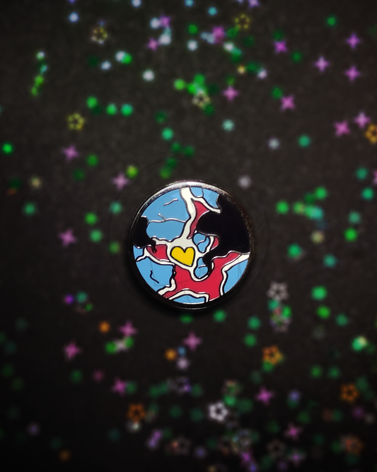 Hard enamel pin of a stylized planet on a dark, blurry background. The pin has the colors of the polyamory flag in it.