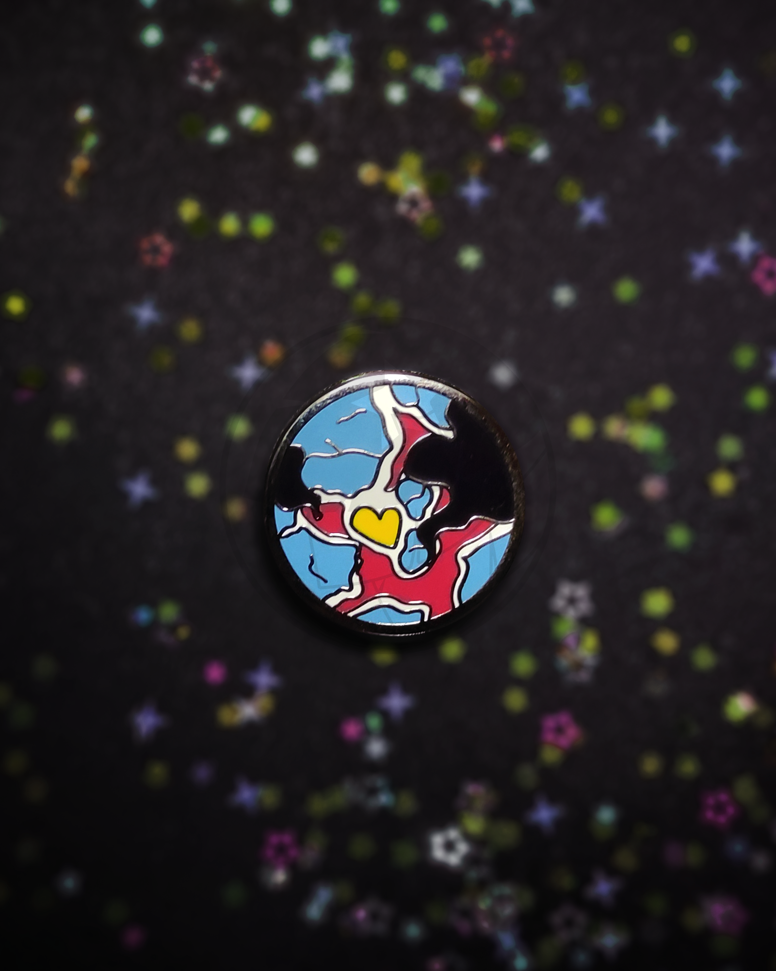 Hard enamel pin of a stylized planet on a dark, blurry background. The pin has the colors of the polyamory flag in it.