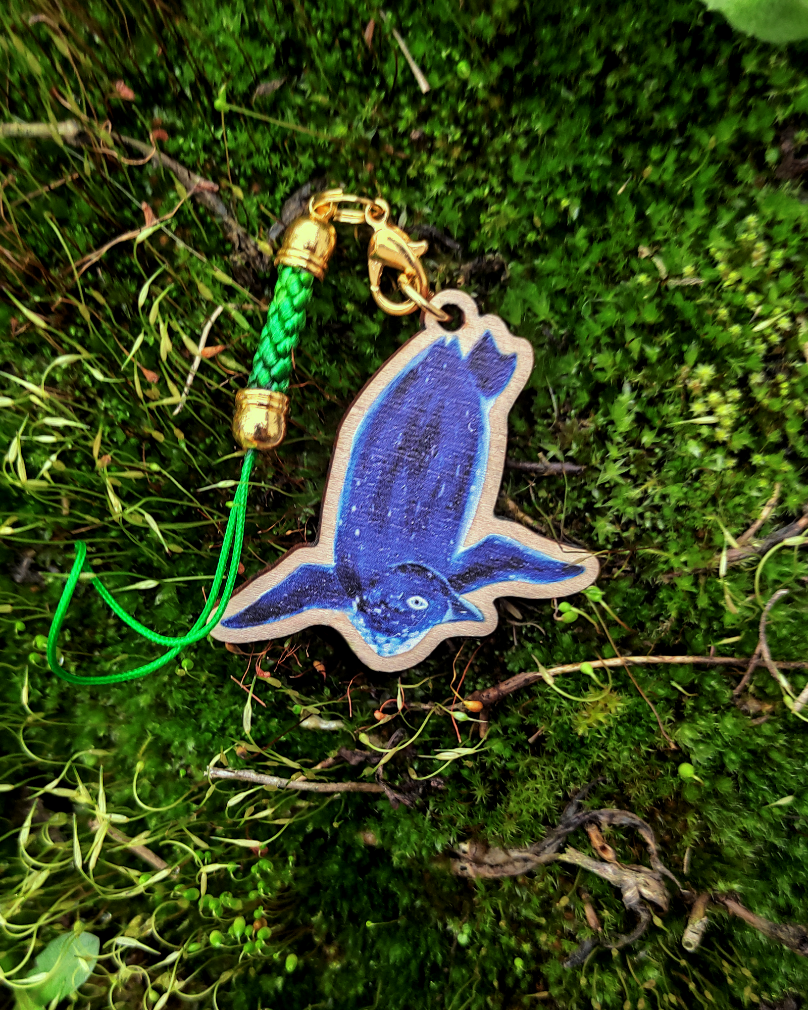 Wooden charm of a Korora on mossy background.