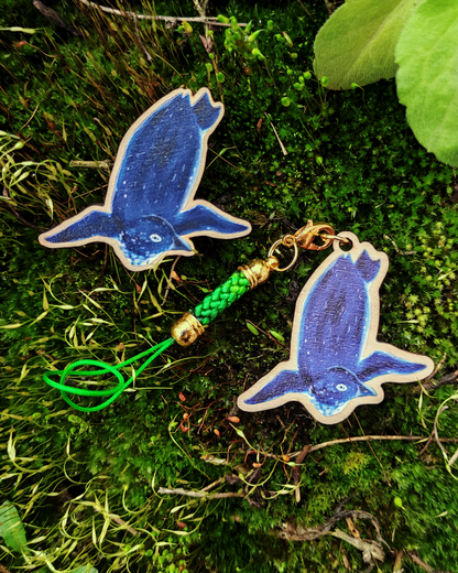 Wooden pin and charm of a Korora on mossy background.