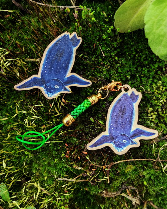 Wooden pin and charm of a Korora on mossy background.