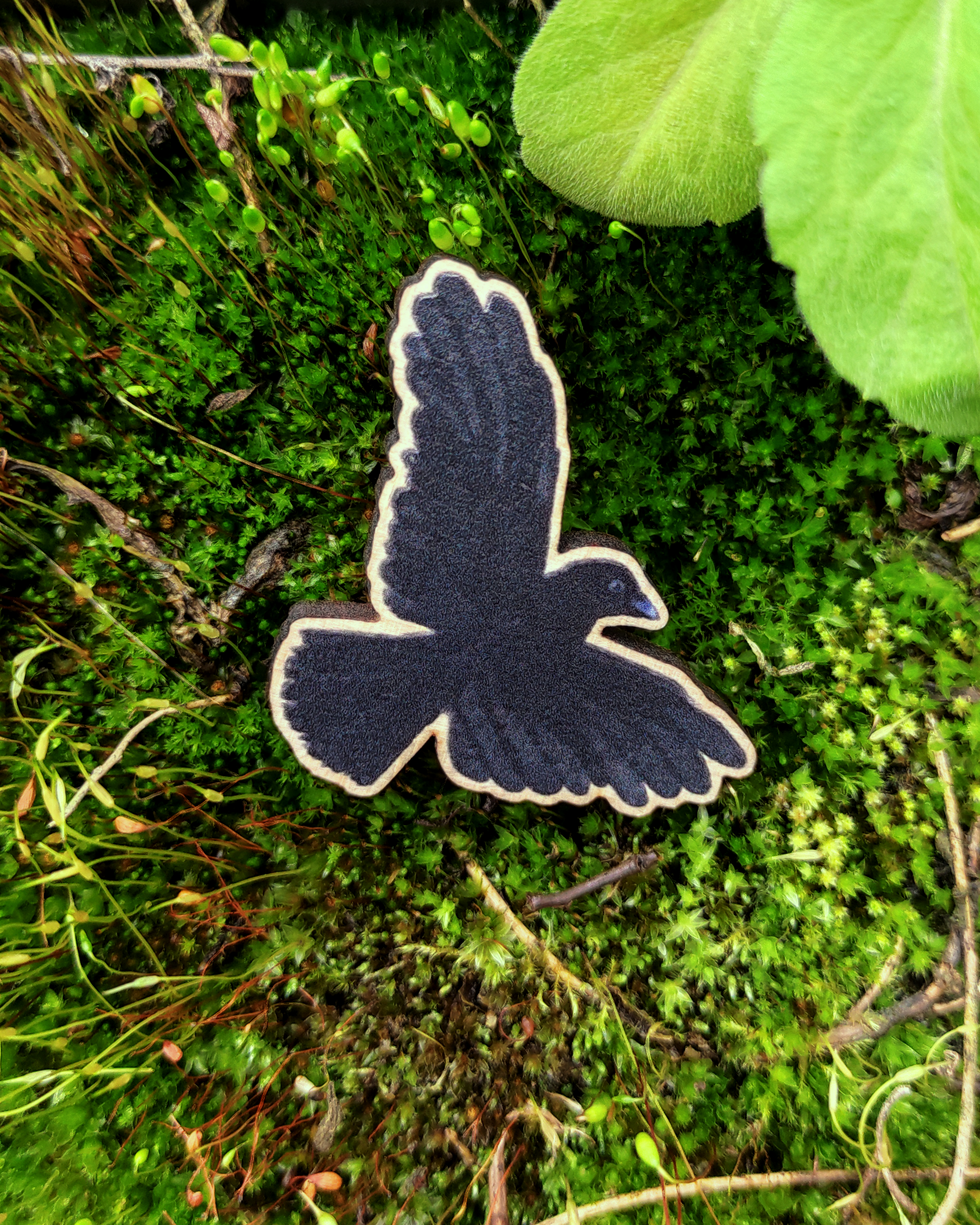Wooden pin of a Carrion Crow on mossy background.