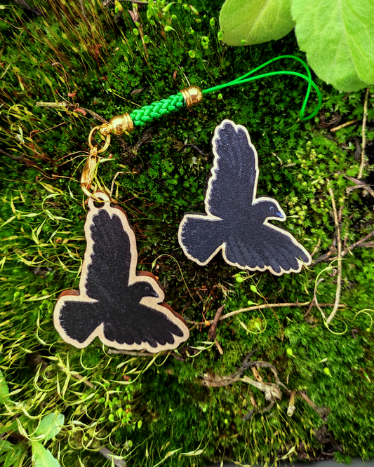 Wooden pin and charm of a Carrion Crow on mossy background.