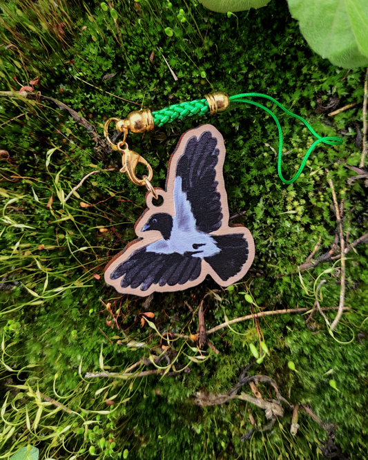 Wooden charm of a Hooded Crow on mossy background.