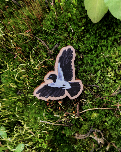 Wooden charm of a Hooded Crow on mossy background.