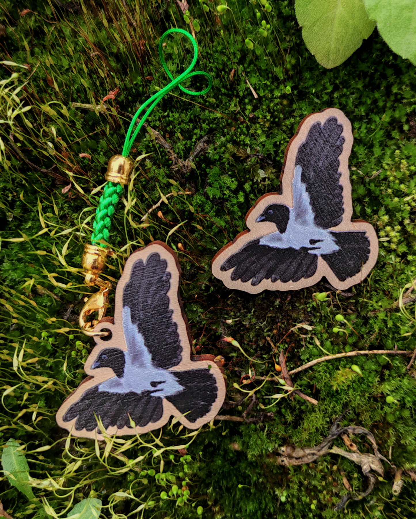 Wooden pin and charm of a Hooded Crow on mossy background.