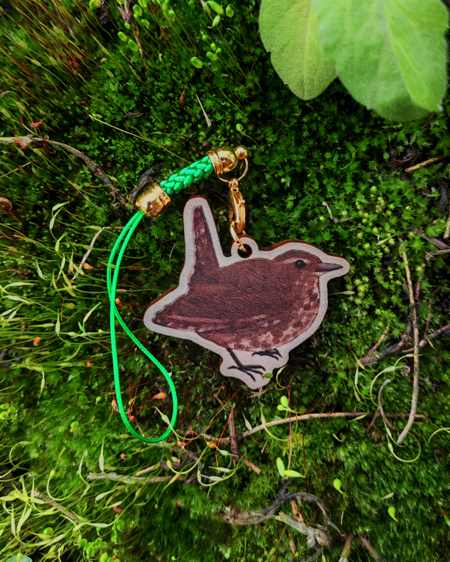 Wooden charm of a Wren on mossy background.