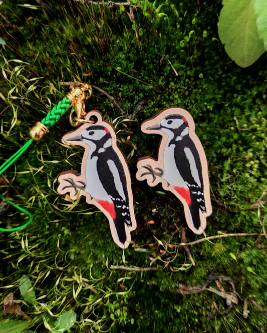 Wooden pin and charm of a Great Spotted Woodpecker on mossy background.