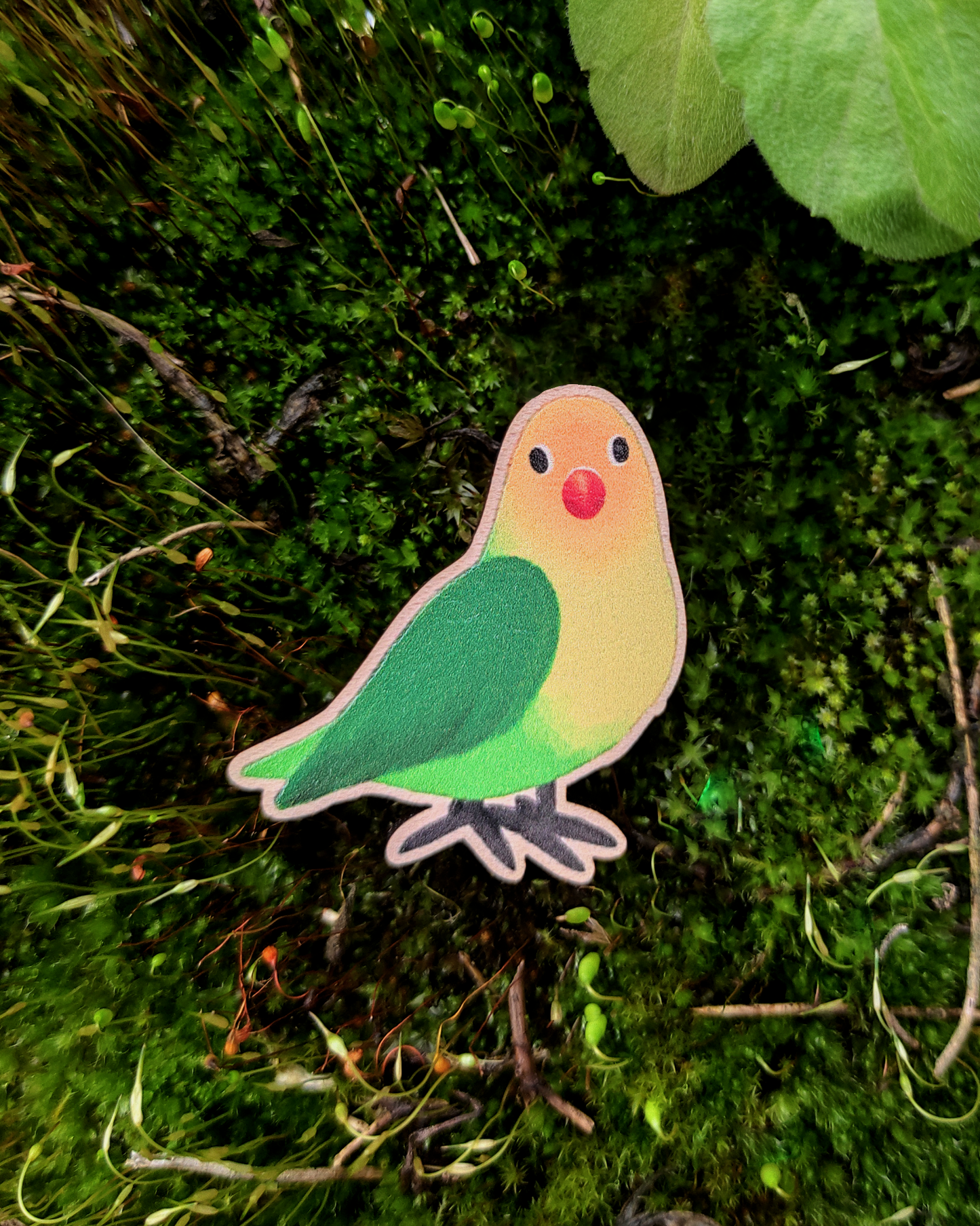 Wooden pin of a Lovebird on mossy background.