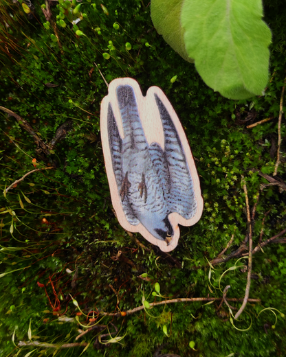 Wooden charm of a Peregrine Falcon on mossy background.