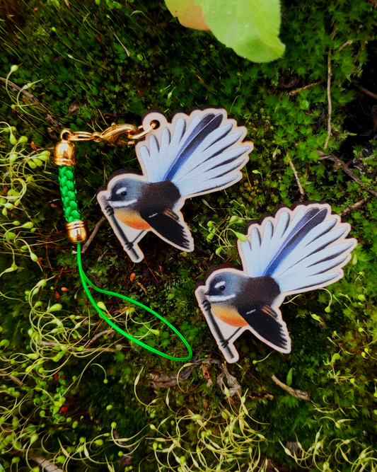Wooden pin and charm of a New Zealand Fantail on mossy background.