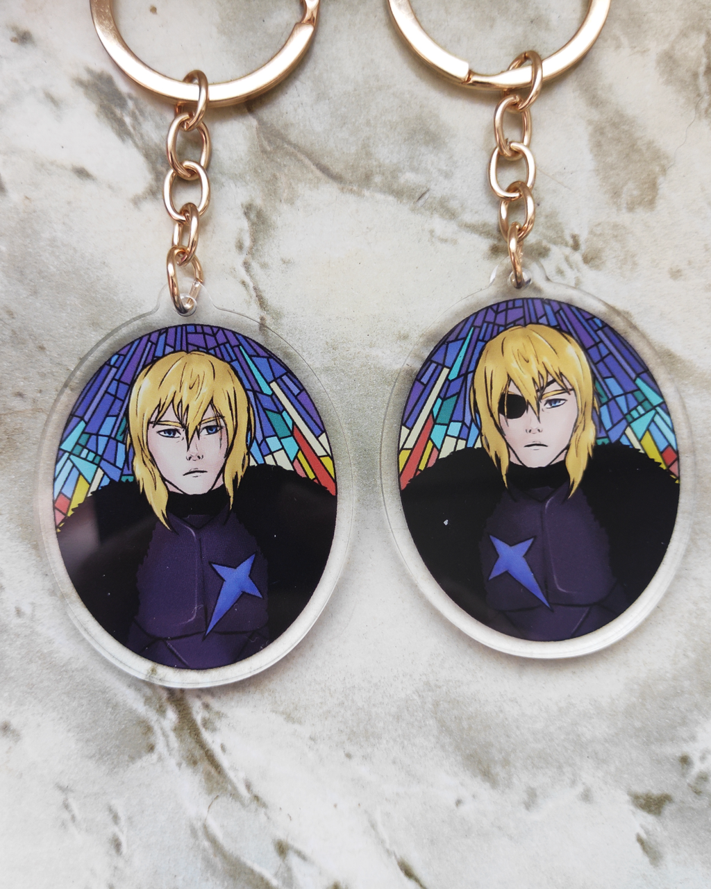 Two keychains of Dimitri of Fire emblem on a marble surface. Each side shows a different version of him.