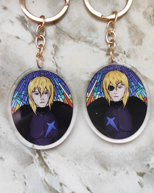 Two keychains of Dimitri of Fire emblem on a marble surface. Each side shows a different version of him.